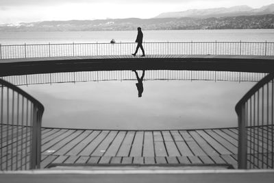 Silhouette man walking on pier by sea against sky