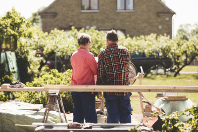 Rear view of senior couple standing by wooden plank against house at yard