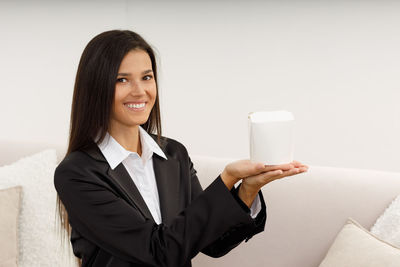Portrait of young businesswoman using mobile phone while standing against white background