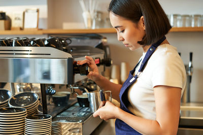 Side view of young woman holding coffee at home