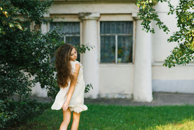 A young woman with long hair runs through the grass in the city park in summer, her hair fluttering