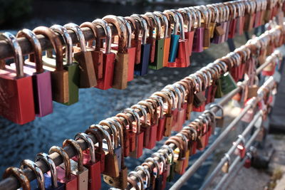 Multi colored padlocks hanging on railing at bridge