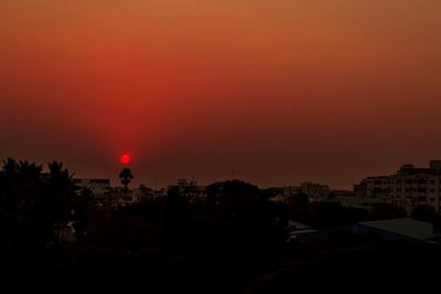 Silhouette trees and cityscape against sky during sunset