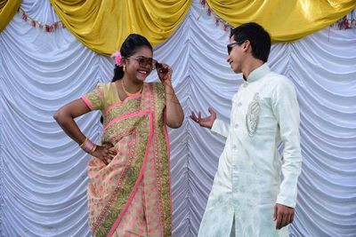 Young couple wearing sunglasses while standing against curtain