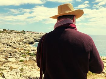 Rear view of man wearing hat at beach against sky