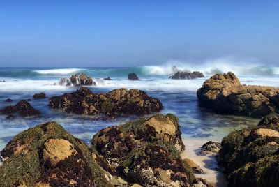 Beautiful scenic landscape of waves crashing on rocky beach along pacific grove coastline, blue sky