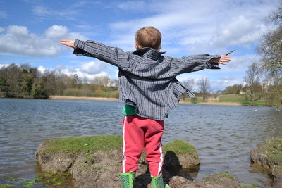 Rear view of boy standing by lake against sky