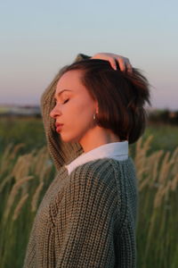 Young woman looking away while standing on field against sky during sunset