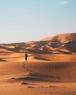 Woman on sand dune in desert against sky