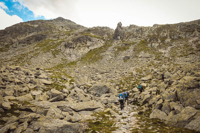 Rear view of backpackers walking towards mountain against sky