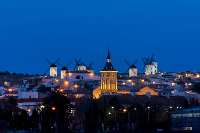 Illuminated buildings against blue sky at night