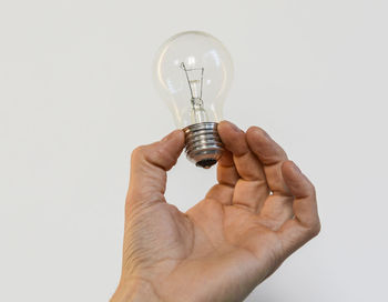 Close-up of hand holding light bulb over white background