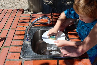 Child's hands wash a plate with a dishwashing sponge. father helps his son wash the dishes.