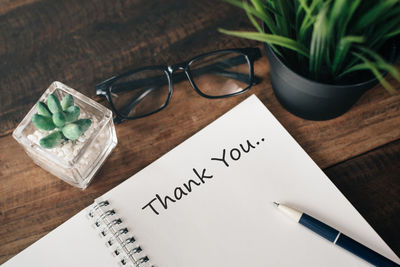 High angle view of thank you text on paper with plant and eyeglasses on wooden table