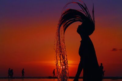 Silhouette teenage girl tossing hair against sky at beach