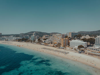 Aerial view of buildings by sea against clear blue sky