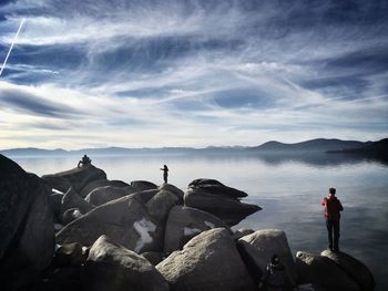 People on rocks by lake against sky