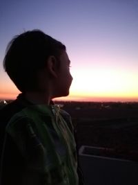 Boy looking away against sky during sunset