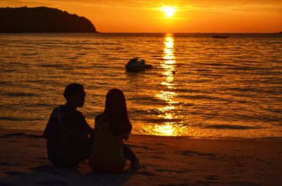 Silhouette couple sitting at beach during sunset