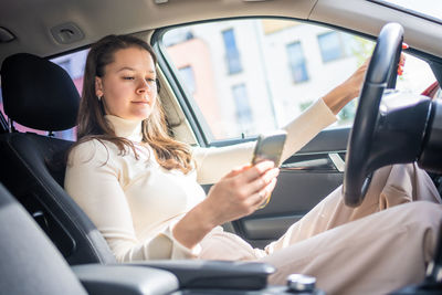 Young woman using mobile phone while sitting in car