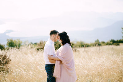 Side view of couple standing on field against sky