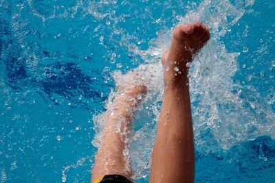 Low section of woman splashing water in swimming pool