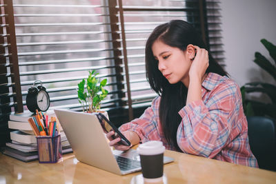 Young woman using mobile phone while sitting on table