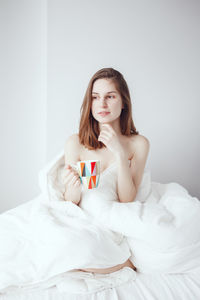 Young woman holding mug while sitting on bed