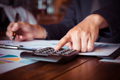 Midsection of businessman calculating on table