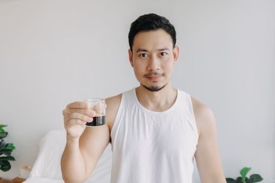 Portrait of young woman drinking water while standing against white background