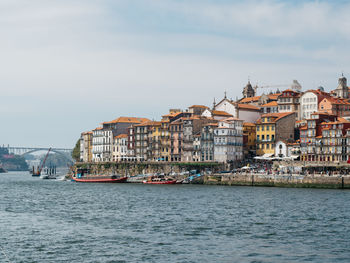 Sailboats in sea by buildings against sky