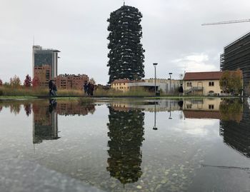 Reflection of buildings in lake against sky in city