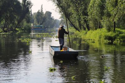 Man standing in boat on lake against trees