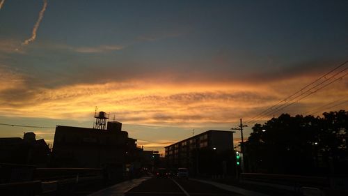 Road by silhouette city against sky during sunset