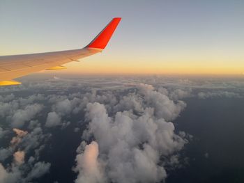 Airplane wing over clouds against sky during sunset