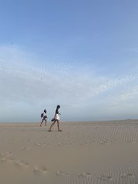 Two women on sand against sky