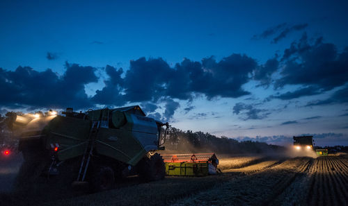 Low angle view of combine harvesters against sky during dusk