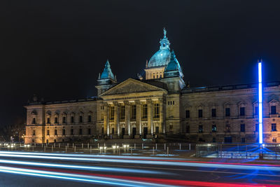 Light trails on street by illuminated federal administrative court against clear sky at night