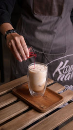 Midsection of woman pouring syrup in drink on table