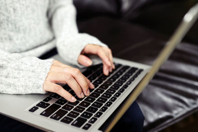 Midsection of woman using laptop sitting on sofa at home