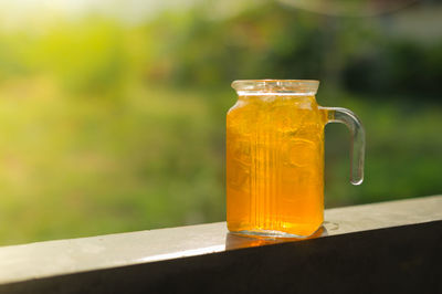 Close-up of orange juice in glass jar on railing