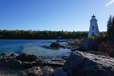 Lighthouse by sea against clear sky