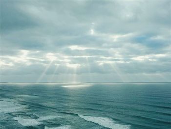 Scenic view of sunbeams streaming from clouds over sea