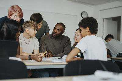 Male teacher teaching boys and girls with non-binary person in classroom