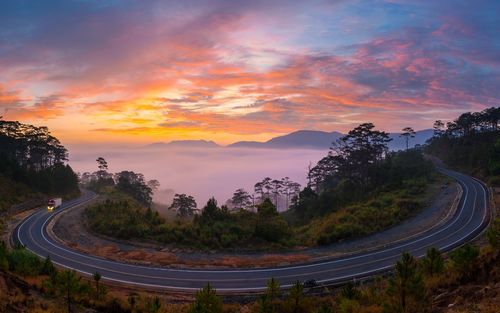 Road amidst trees against sky during sunset