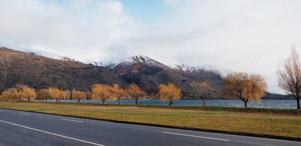 Empty road by lake wanaka against mountains during autumn