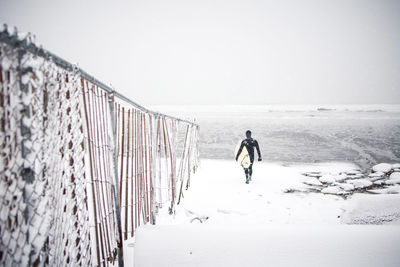 Surfer walks along maine beach during winter snow storm