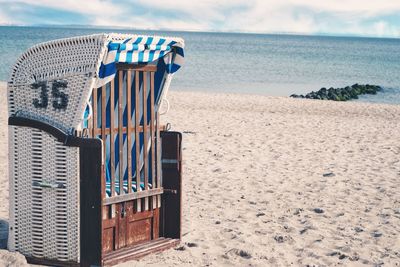 Hooded chairs on beach against sky