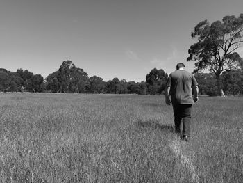 Rear view of man walking on field against sky