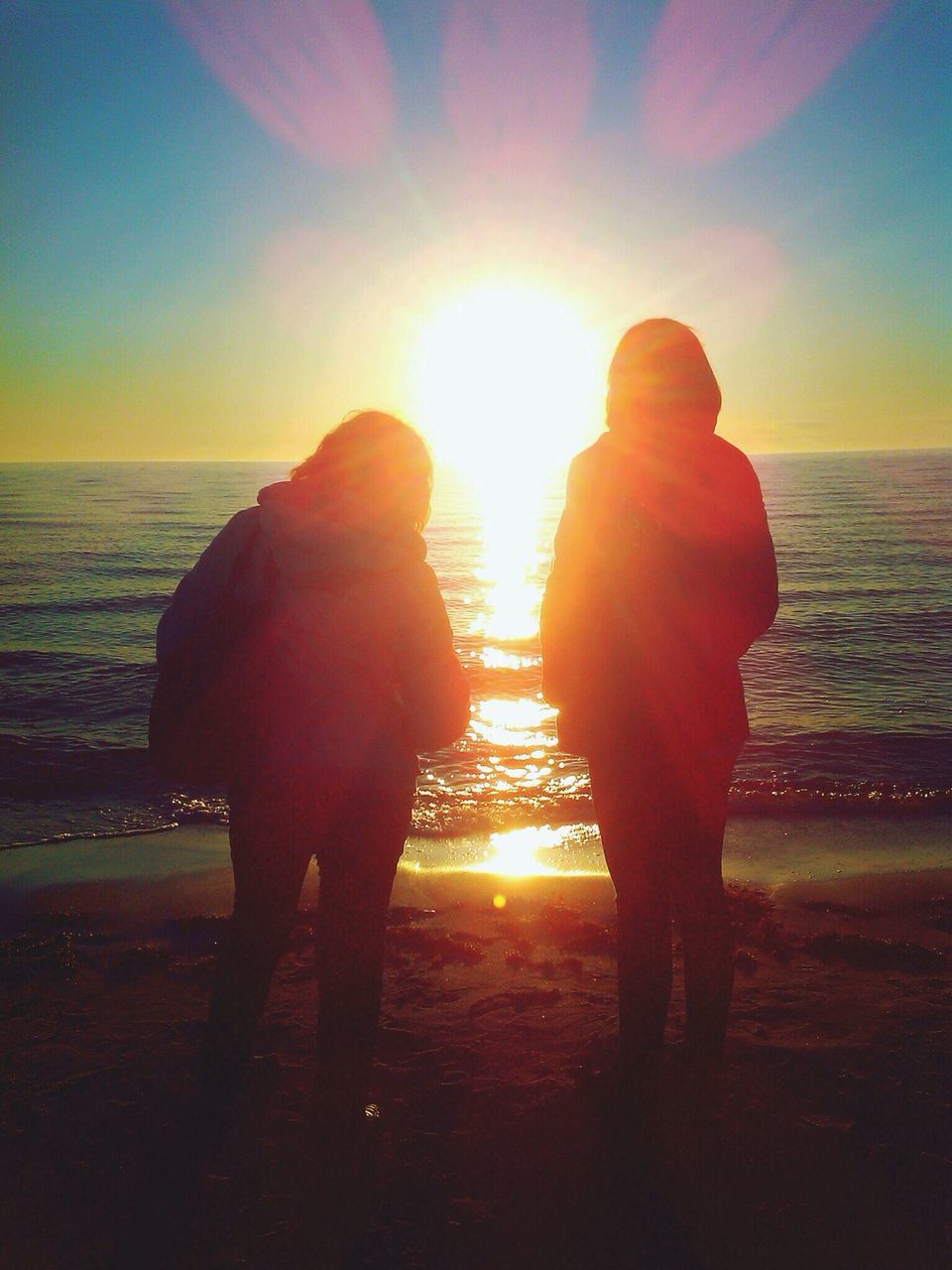 sunset, sun, silhouette, sea, water, orange color, sunlight, sky, leisure activity, lifestyles, horizon over water, lens flare, rear view, beauty in nature, person, beach, sunbeam, standing